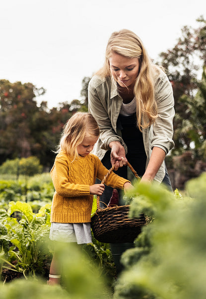 Cheerful young mother reaping fresh vegetables with her daughter