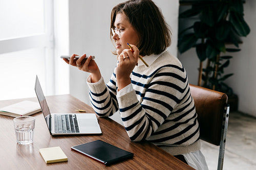 At the office desk, the woman handles multitasking with a laptop and phone