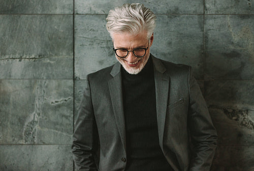 Smiling mature businessman standing against grey wall