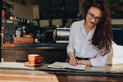 Woman sitting in the cafe writing notes in her diary