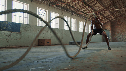 Muscular man exercising with battle ropes in gym