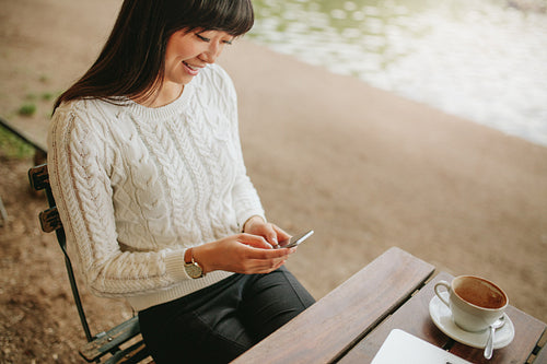 Woman sitting at cafe using mobile phone and smiling
