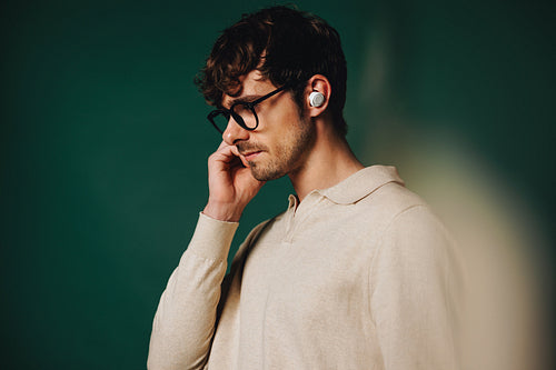 Young pensive man in glasses adjusting earbuds in studio portrait