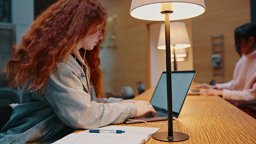 Female college student working on her dissertation in a library, using online articles for her research