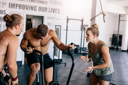 Man doing  intense workout on gym bike with personal coach