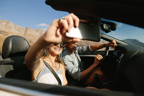 Couple on road trip in convertible car taking selfie