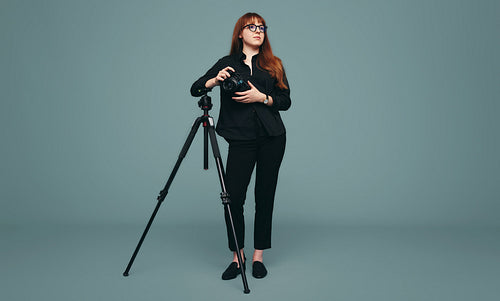 Pensive photographer standing next to her tripod in a studio