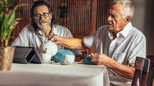 Senior friends relaxing at home having tea while knitting