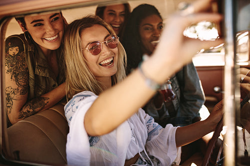 Woman driving a car and making selfie with friends