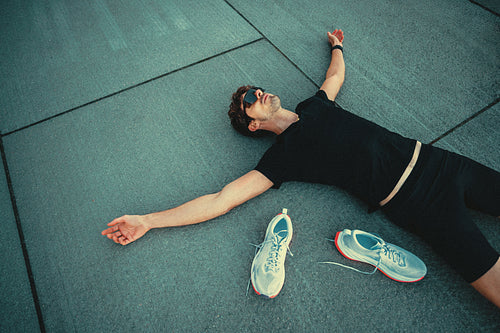Runner recovering on pavement after intense workout with his shoes removed