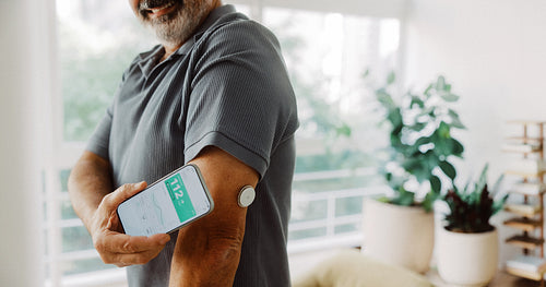 Senior man scans glucose sensor with smartphone at home