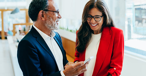 Smiling business professionals discussing information on a smartphone during a break