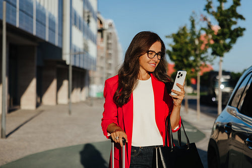 Middle-aged woman checking her phone while walking outdoors carrying a handbag