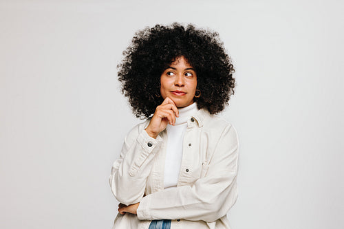 Pensive woman with Afro hair standing against a white background