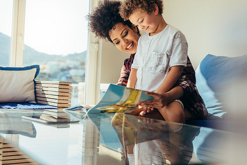 Mother and son reading a book sitting on a couch at home