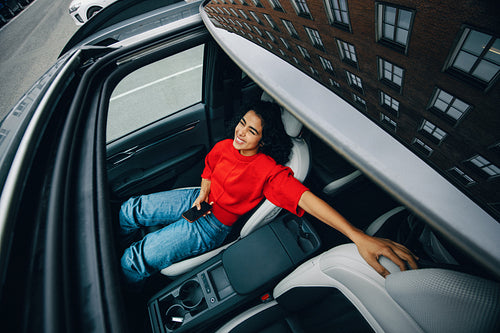 In the car, the woman takes a travel break as a passenger with her smartphone