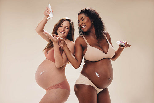 Pregnant moms having fun with applying stretch mark cream