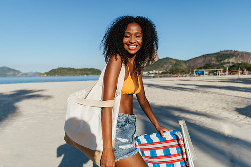 Smiling young woman in swimsuit with beach chair at sunny seaside