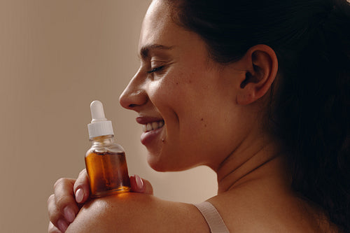 Smiling woman holding dropper bottle of facial oil on shoulder