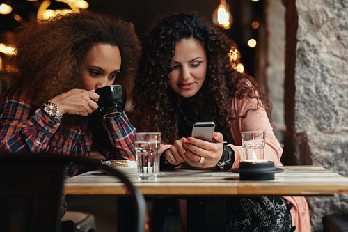 Young friends sitting in a cafe looking at a smartphone