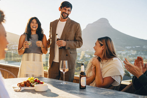 Host couple sharing laughter and drinks with friends at a terrace dinner gathering