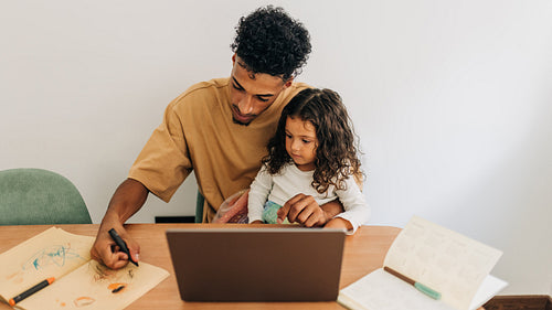Dad showing his little girl how to draw with a colour pencil