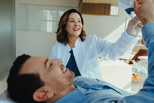 Female dentist discusses treatment plan with male patient holding dental item