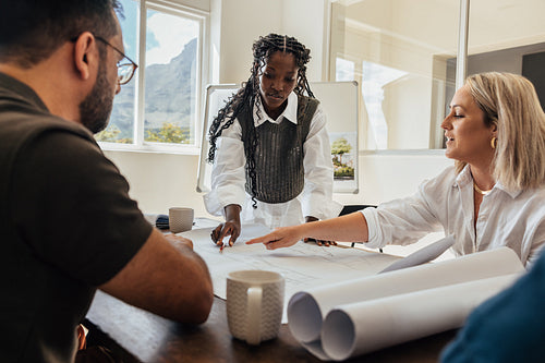 Architects discussing designs at office table with plan drawings and teamwork dynamics.