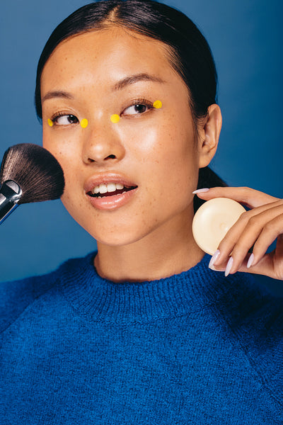 All things beauty: Young woman holding a makeup brush and foundation in a studio