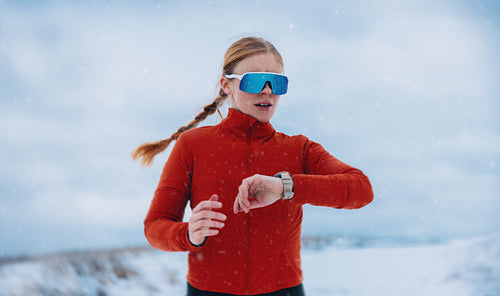 Woman checking smartwatch during winter running training in falling snow