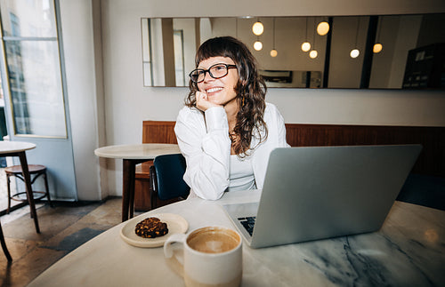 Woman working on laptop in cafe, candid smile