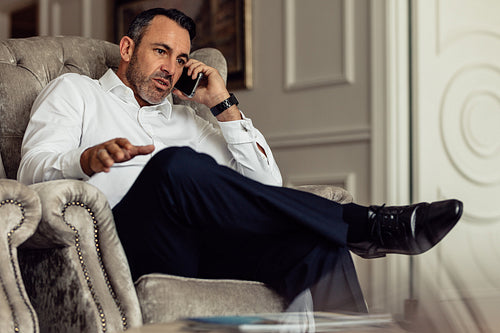 Businessman sitting on couch and talking on smartphone