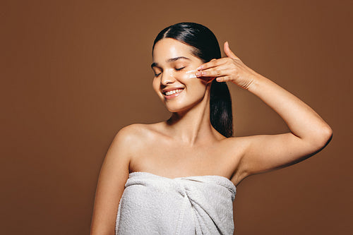 Female skincare and self-care. Happy young woman applies facial cream in a studio