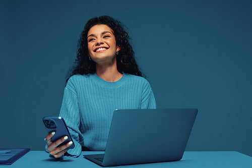 Buyer smiling in monochromatic studio using smartphone and laptop