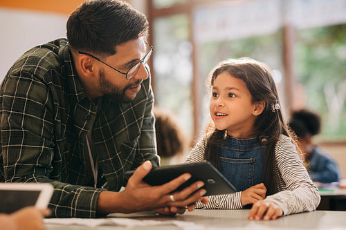 Male teacher talking to his student while holding a digital tablet
