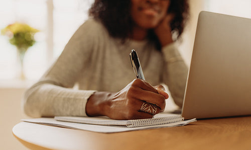 Woman making notes looking at laptop working from home