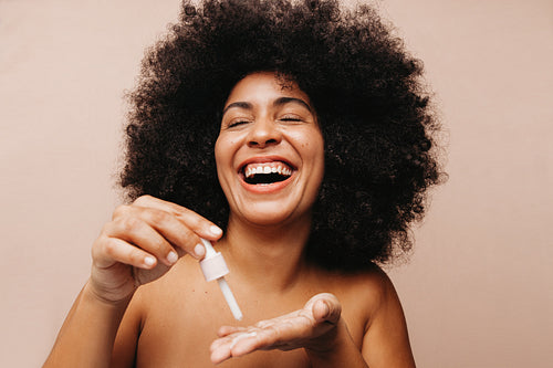 Happy young woman dropping face serum onto her palm