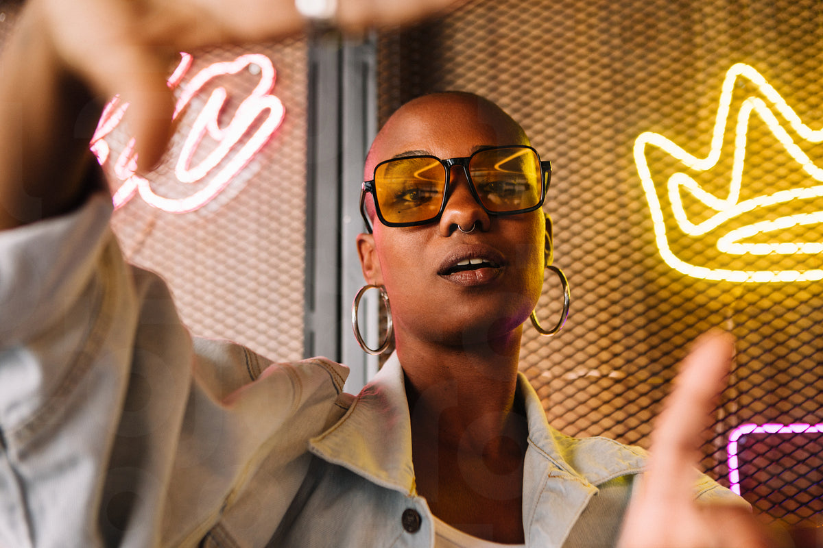 Stylish woman with sunglasses posing in front of neon lights in modern ...