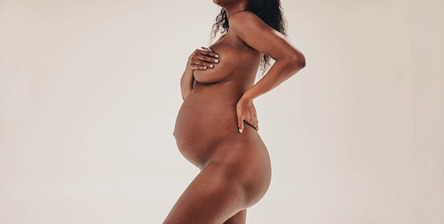 Confident dark-skinned woman displaying her pregnancy body in the third trimester