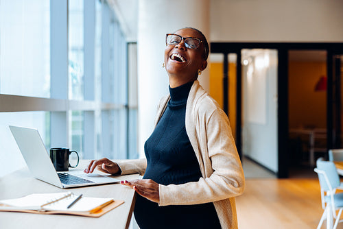 Smiling pregnant woman working on a laptop in a bright office setting