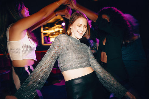 Group of friends dancing joyfully at a nightclub party with vibrant lights