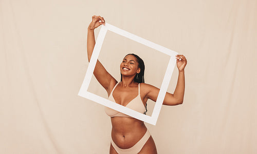 Playful young woman smiling through a picture frame in a studio