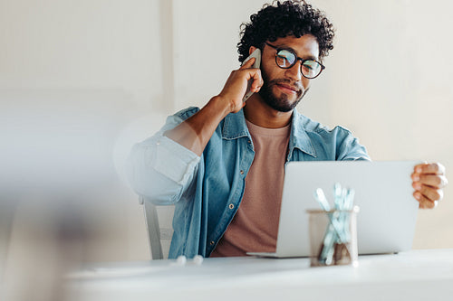 Focused young man working on laptop while on a phone call