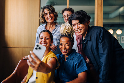 Group of diverse colleagues smiling and taking a selfie indoors