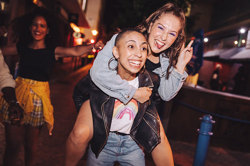 Young woman piggybacking her friend outdoors at night