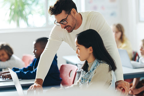 School teacher helping a young student with a coding lesson in a classroom