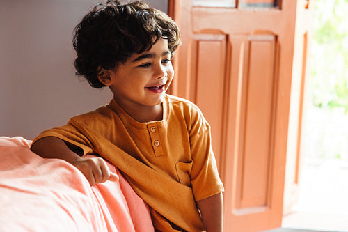 Cheerful young Latin American boy smiling indoors beside an open door