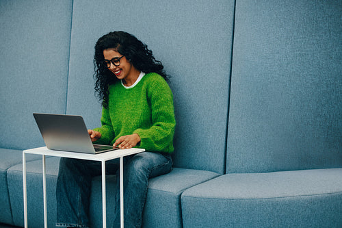 Using a laptop, the woman relaxes on the sofa indoors for remote work