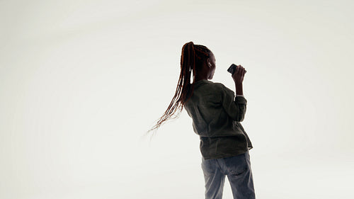 Young black woman dancing happily with smartphone and earbuds in a bright studio
