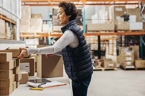 Female warehouse worker packing cardboard boxes